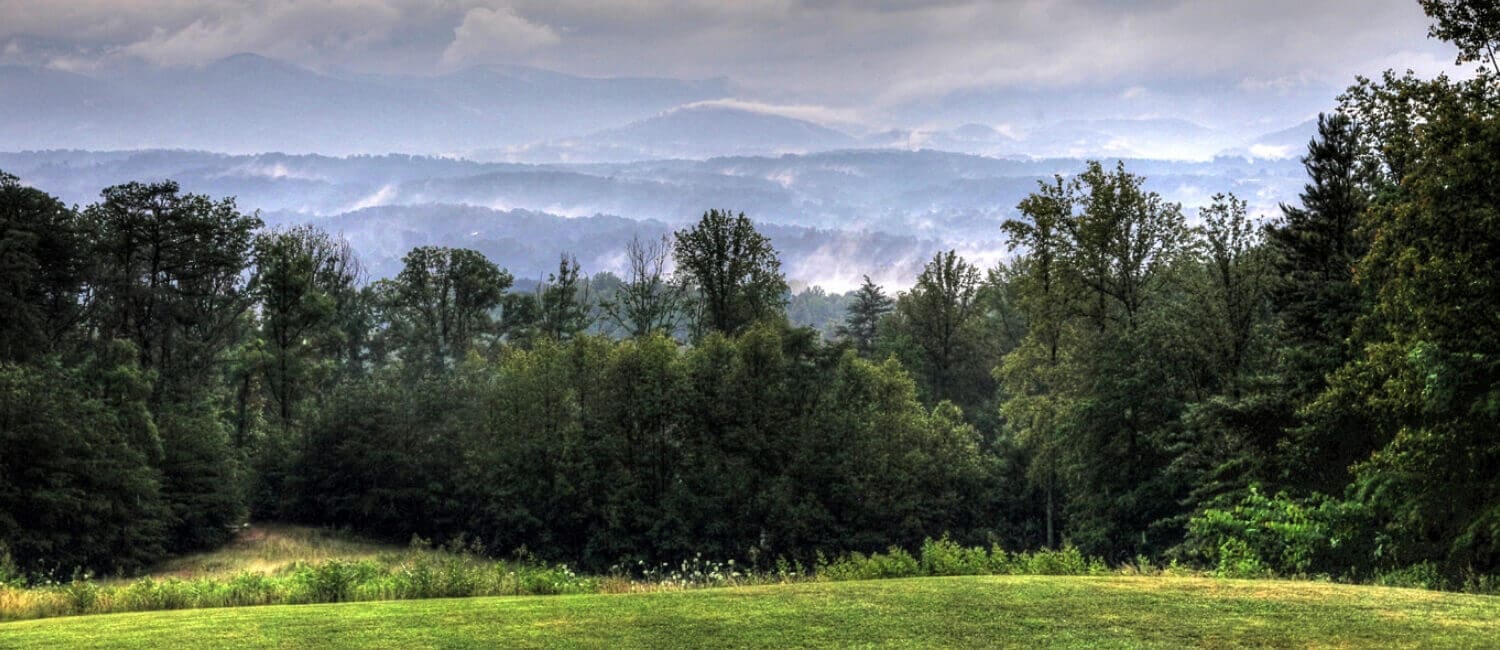 View from the porch looking out on mountains, green grass and trees, and cloud cover